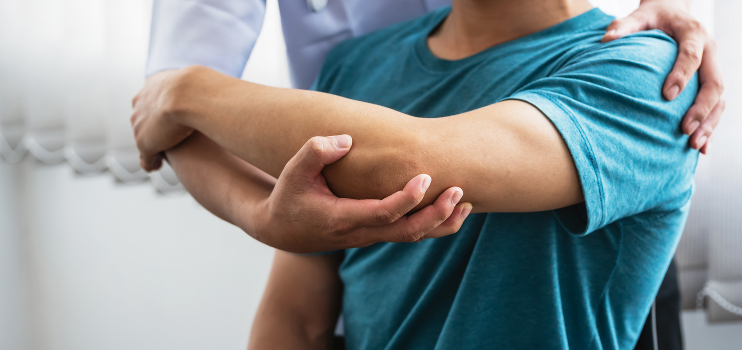Man physiotherapist stretching shoulder and arm patient at a clinic.